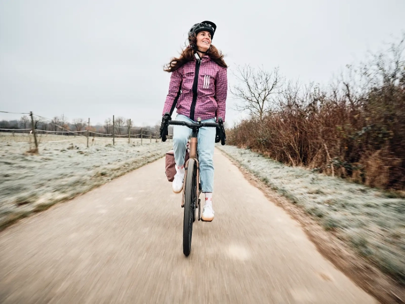 Junge Frau fährt ohne Hände auf dem Gravelbike über den winterlichen Wirtschaftsweg