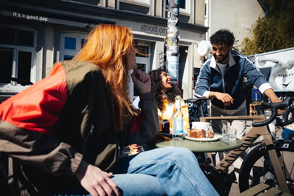 Junge Leute im Cafe. Ein Freund zeigt sein Gravelbike von JobRad
