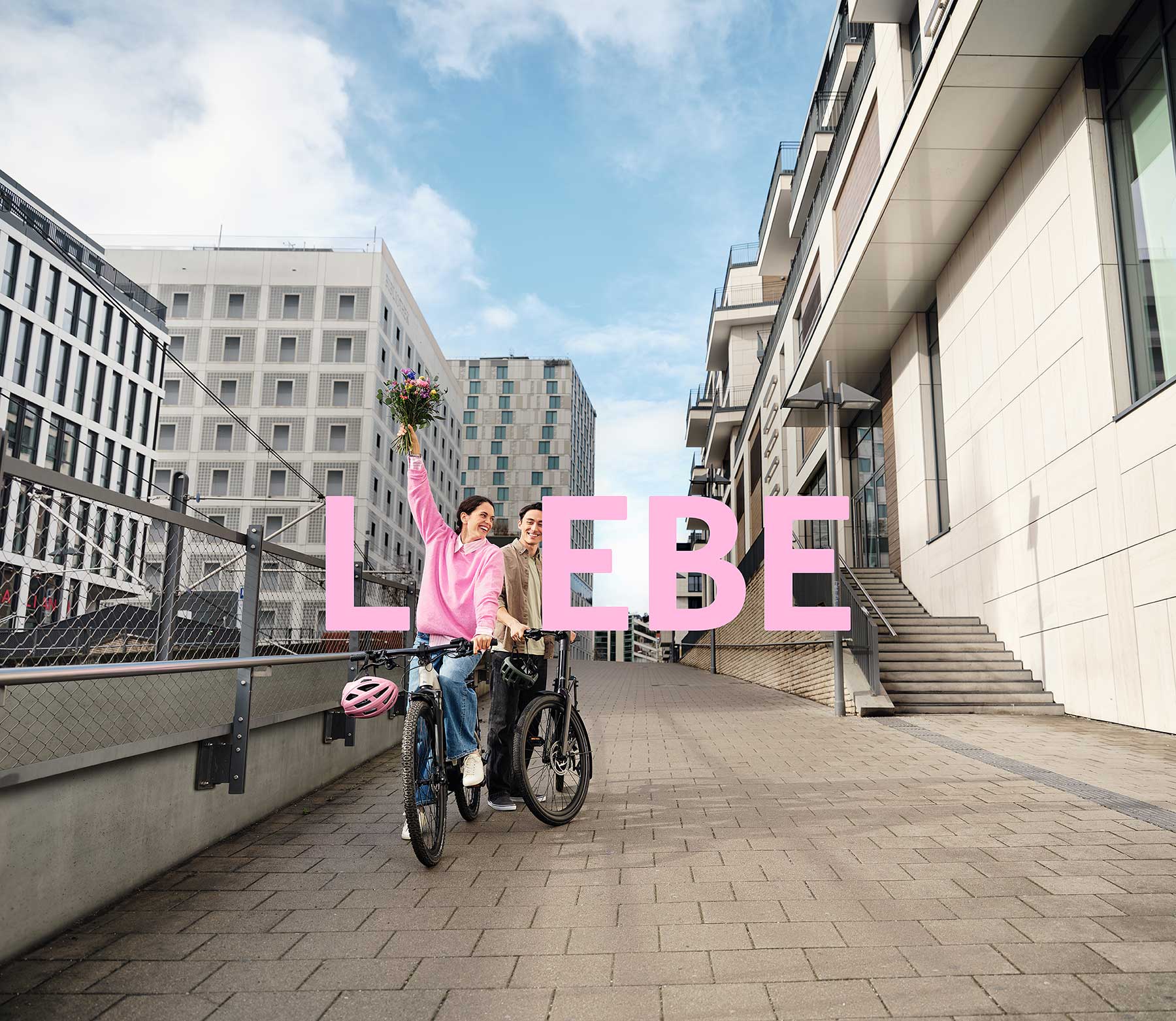 2 JobRadler:innen auf einem Fahrrad in einem urbanen Umfeld mit einem Blumenstrauß. 2 JobRadler:innen auf einem Fahrrad in einem urbanen Umfeld mit einem Blumenstrauß.